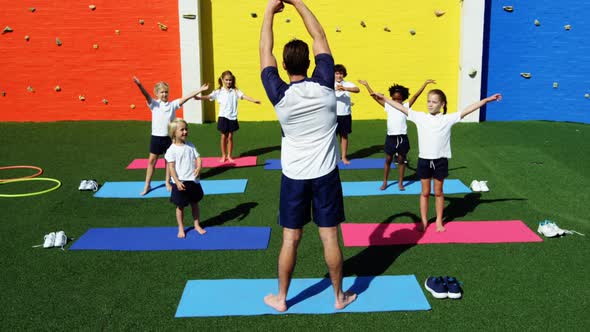 Yoga instructor instructing children in performing exercise