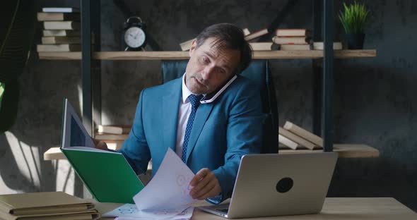 Multitasking Middleaged Business Man Conducts Business Negotiations Using Mobile Phone While Working