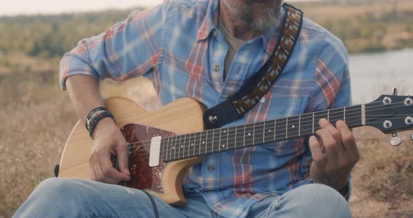 Man Plays the Electric Guitar on Meadow