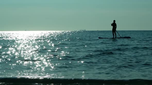 Sup board. A beautiful woman on a surfboard with a paddle floats in the open sea at sunset.