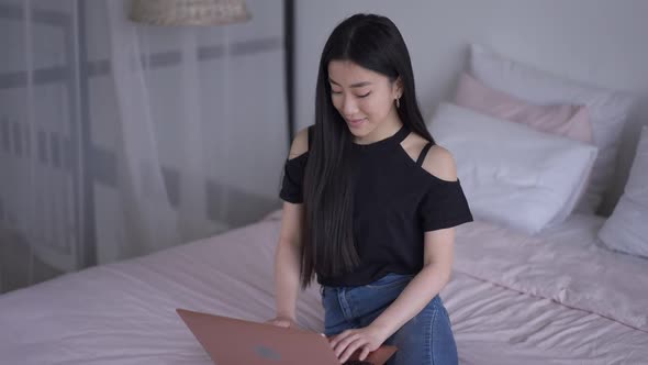 Young Beautiful Slim Confident Woman Sitting on Bed Typing on Laptop Keyboard