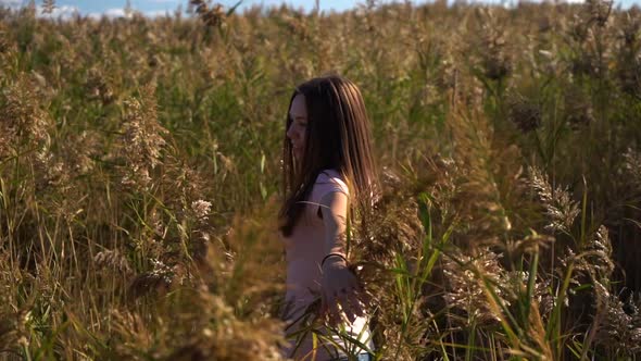 Young Woman or Girl in Pink T-shirt and Blue Jeans Spinning in Slow Motion in Field of Reed or Cane