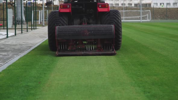 Worker on a Red Lawn Mower Pierces the Lawn Grass in a Football Stadium