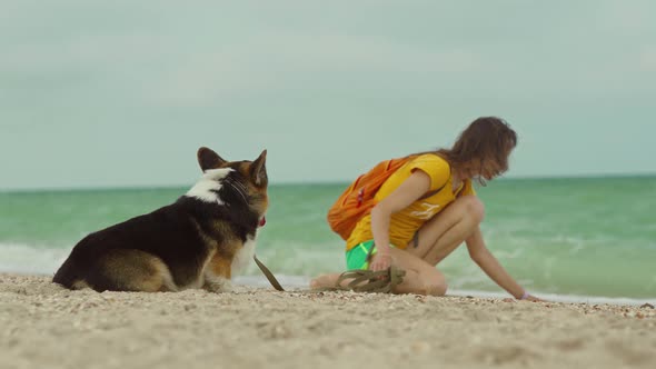 Attractive Young Woman Spending Time Together with Her Pet Cute Corgi Dog Outdoors at Sandy Sea
