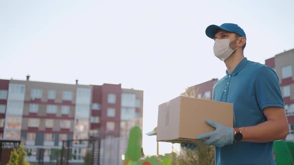 An Young Mailman Courier with a Protective Mask and Gloves is Delivering a Parcel Directly to a