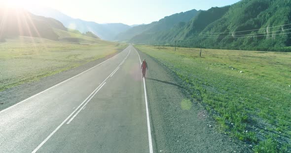 Flight Over Hitchhiker Tourist Walking on Asphalt Road. Huge Rural Valley at Summer Day. Backpack