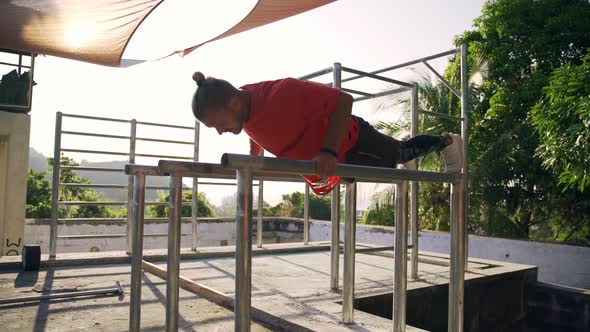 Athletic Man Working Out Outdoor, Doing Pushups on the Uneven Bars.