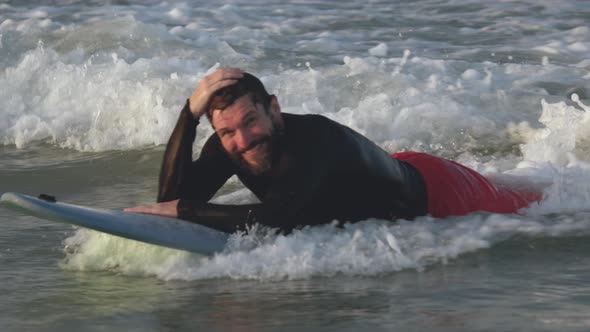 Portrait of a Handsome Senior Sportsman with a Beard on the Waves Lying on a Surfboard Smiling