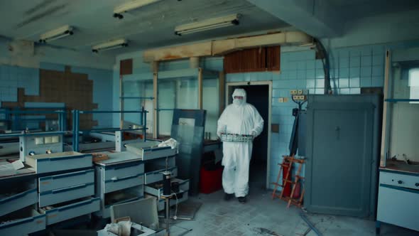 A man in a protective suit and mask enters the audience holding a box of test tubes.