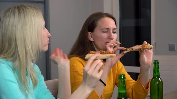 Two best happy girlfriends at home in kitchen eating pizza and drinking beer.