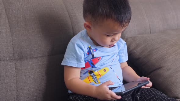 Little Boy Playing Smartphone On Sofa