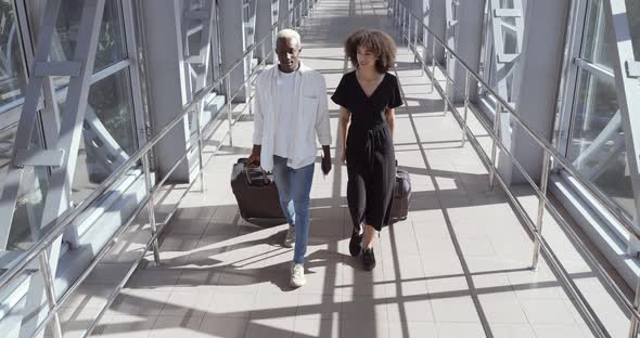 African Woman and American Black Man Walk Together Talking, Carry Suitcases, Enter Airport Terminal