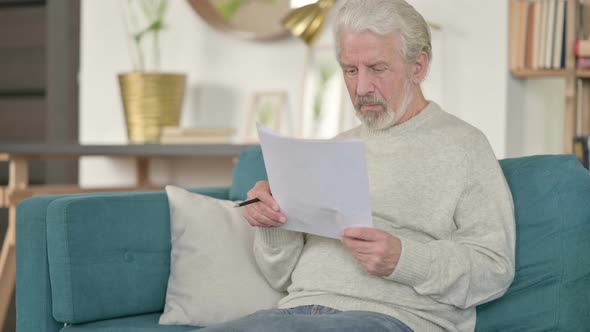 Old Man Reading Documents on Sofa 