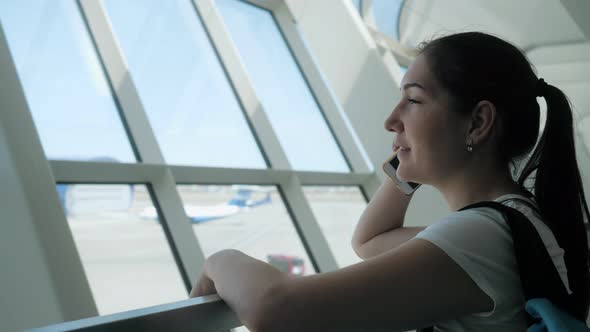 Young Woman Is Talking on Mobile Phone in Airport Terminal in Flight Zone.