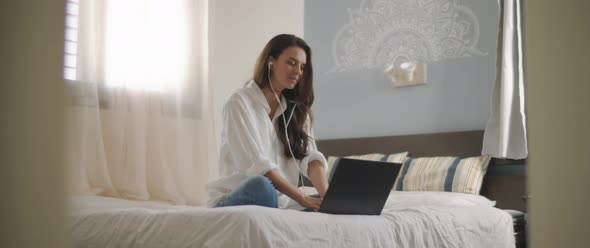 A young woman speaking to someone through earphones while working on her laptop