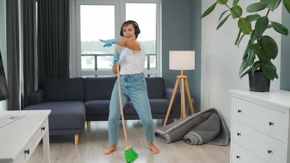 Woman in Headphones Cleans the House and Have Fun Singing with a Broom Like a Star at a Concert