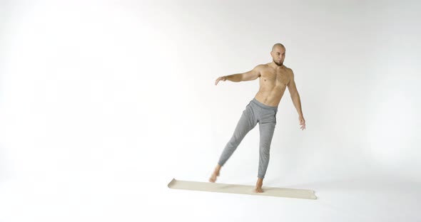 Male Athlete Is Warming Muscles, Lifting Legs Up, Training Alone in Studio with White Background