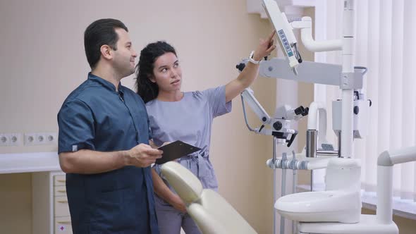 Young Beautiful Caucasian Woman Talking with Middle Eastern Cheerful Man Standing in Dentist Office