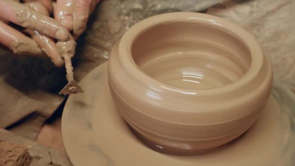 Apprentice scraping off excess clay with triangle knife on ancient revolving pottery wheel