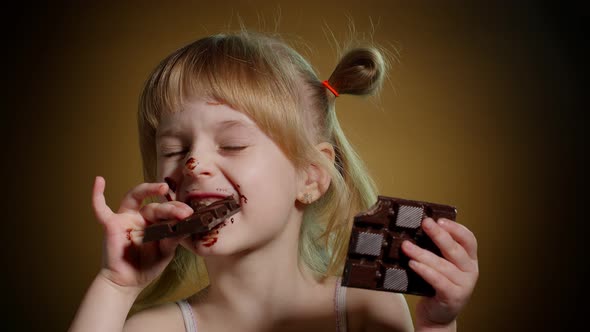 Happy Smiling Little Child Girl Kid Eating Milk Chocolate Bar Dessert Isolated on Dark Background