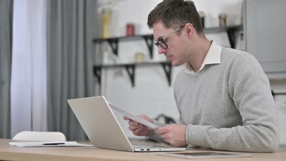 Young Man Using Laptop for Paperwork