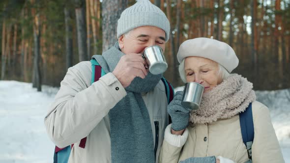 Happy Family Senior Man and Woman Clanging Metal Cups and Drinking Outdoors in Winter Wood