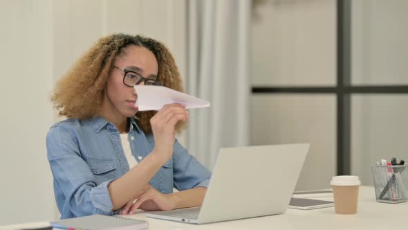 African Woman Flying Paper Plane While Working in Office