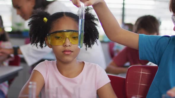 Diverse race schoolchildren wearing protective glasses holding test-tube during chemistry class