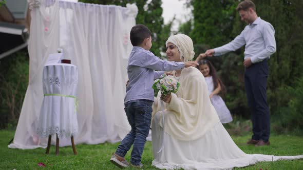 Wide Shot Side View of Happy Little Middle Eastern Boy Hugging Gorgeous Woman in Wedding Dress and