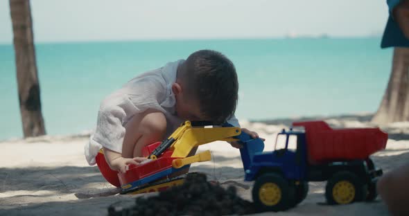 Children Plays with a Plastic Car in the Sand on the Beach