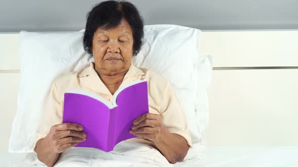 old woman reading a book on bed in bedroom