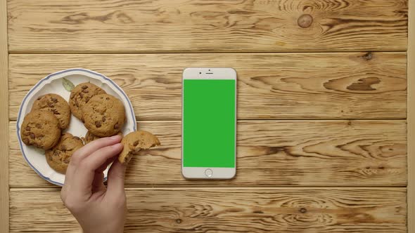 Unrecognizable Person Drinking Coffee and Eating Cookies Near Smartphone