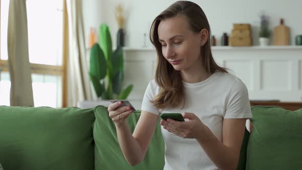 Young Woman Shopping Online with Credit Card and Smartphone While Sitting on Sofa at Home