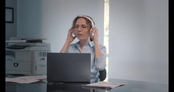 Smiling Caucasian Businesswoman Wearing Headphones Using Laptop at Work