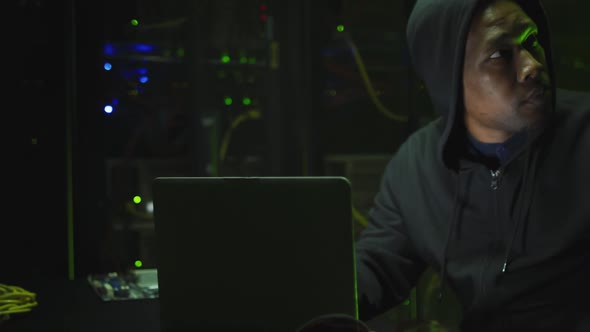 African american male computer hacker using laptop in business server room