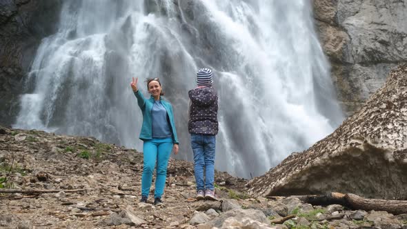 Girl Taking Photos of Mother Near Waterfall