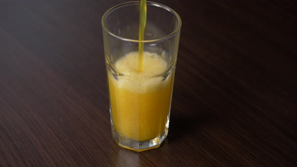 Pouring sparkling orange soda into tall glass on a wooden table