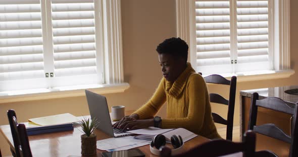 African american woman using laptop and reading documents while working from home