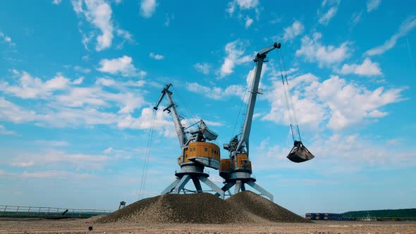 Two Port Cranes Work with Crushed Stones, Moving Them in Piles