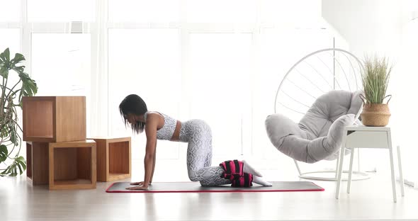 Pretty fitness black woman in sportswear practicing donkey kick exercise with ankle weight.