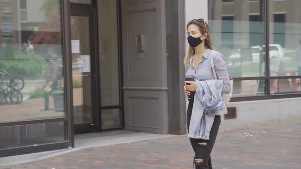 Post covid-19 woman walks on street wearing face mask with reusable water bottle