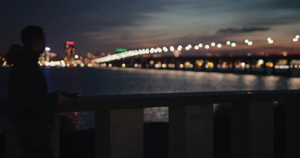 Man Using Smartphone Walking in a City Embankment at Twilight