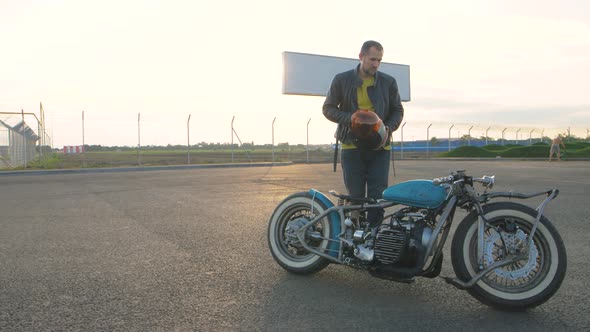 Young Man Biker with Custom Bobber Motorcycle on Street at Sunset