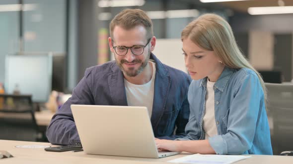 Businessman and Businesswoman Celebrating Success on Laptop in Office