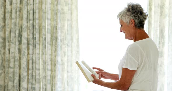 Smiling senior woman reading book in bedroom