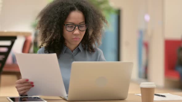 Young African Woman with Laptop Reading Documents