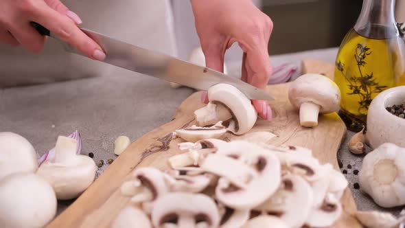 Woman Cuts Champignon Mushrooms with a Knife on a Wooden Cutting Board