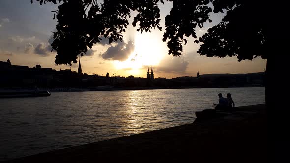 Silhouette of Lovely Couple Sitting on River Pier and Pouring Wine in Glasses