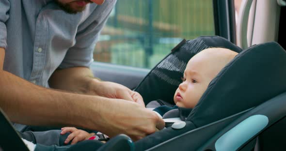 Camera Inside the Car Closeup Baby Boy Sits in the Baby Car Seat Inside of Car Young Bearded Father