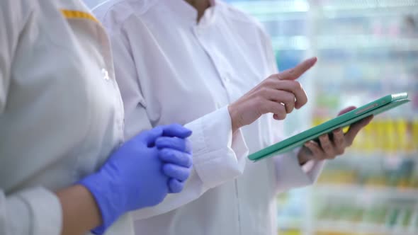 Two Unrecognizable Caucasian Women Gesturing Checking Stock of Medications in Pharmacy Indoors